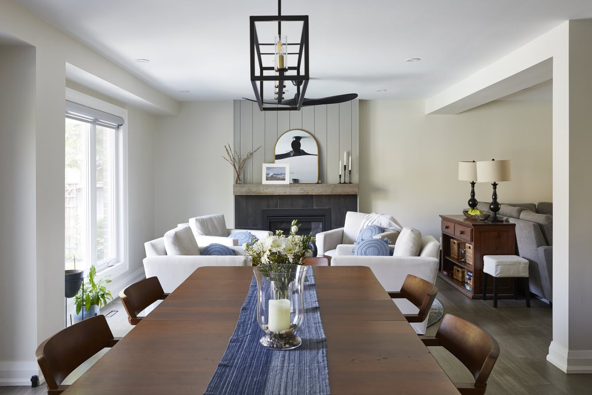 Dining table below black pendant light fixture and living room view in Markham, ON home renovation