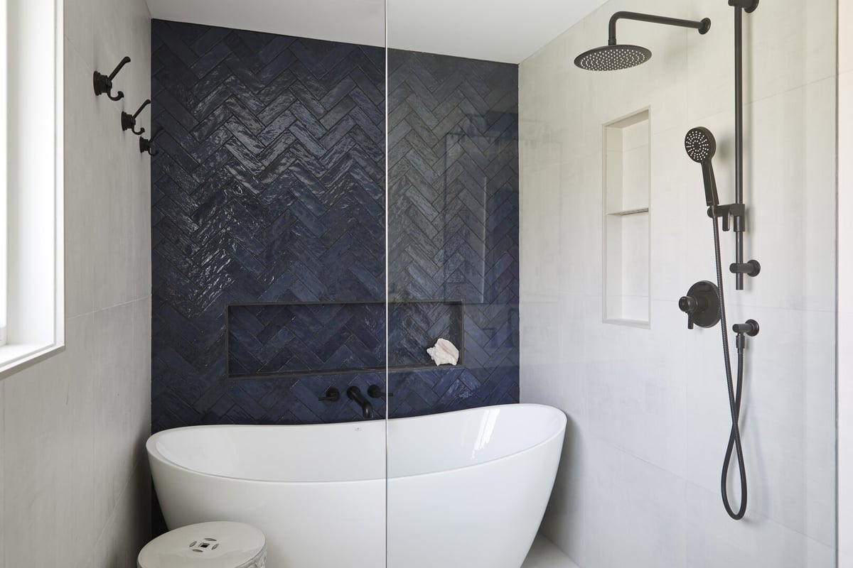 White porcelain tub in wet room with blue herringbone pattern accent wall and black shower fixtures